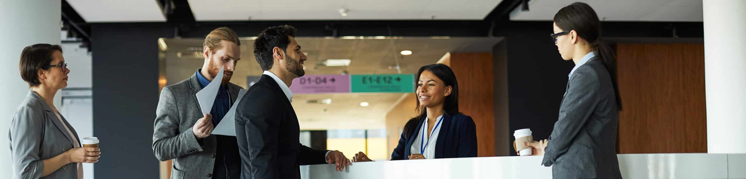 Handsome mixed race businessman with travel bag standing at registration counter and talking to receptionist while checking in to hotel